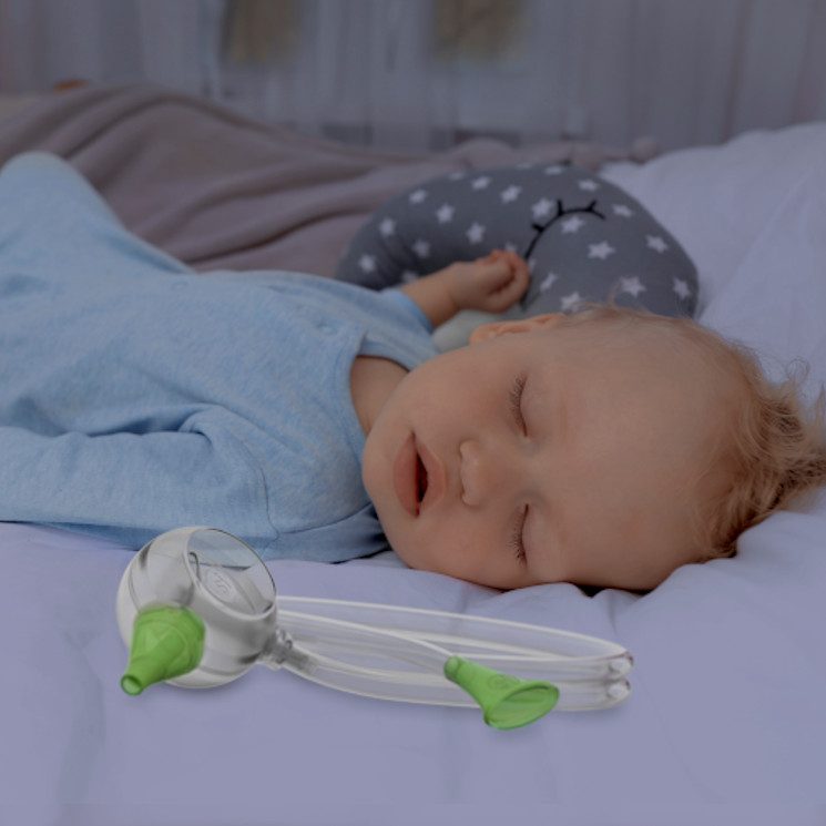 A baby boy sleeping peacefully in his bed next to the Nosiboo Eco Manual Nasal Aspirator