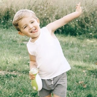 A happy boy holding the Nosiboo Go Portable Nasal Aspirator while playing outside in the park