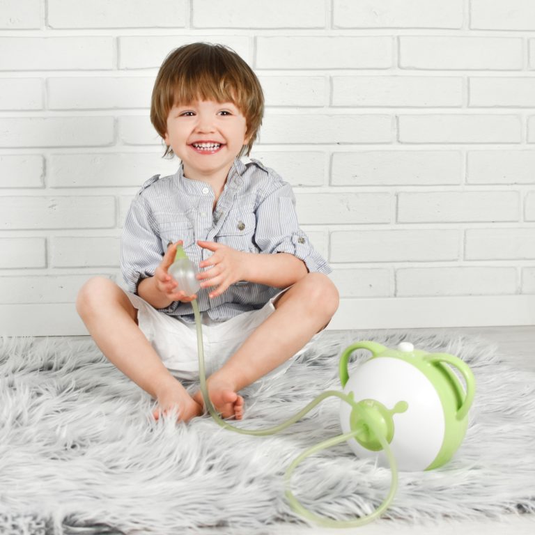 Uśmiechnięty chłopiec trzyma w ręce aspirator elektryczny do nosa Nosiboo Pro