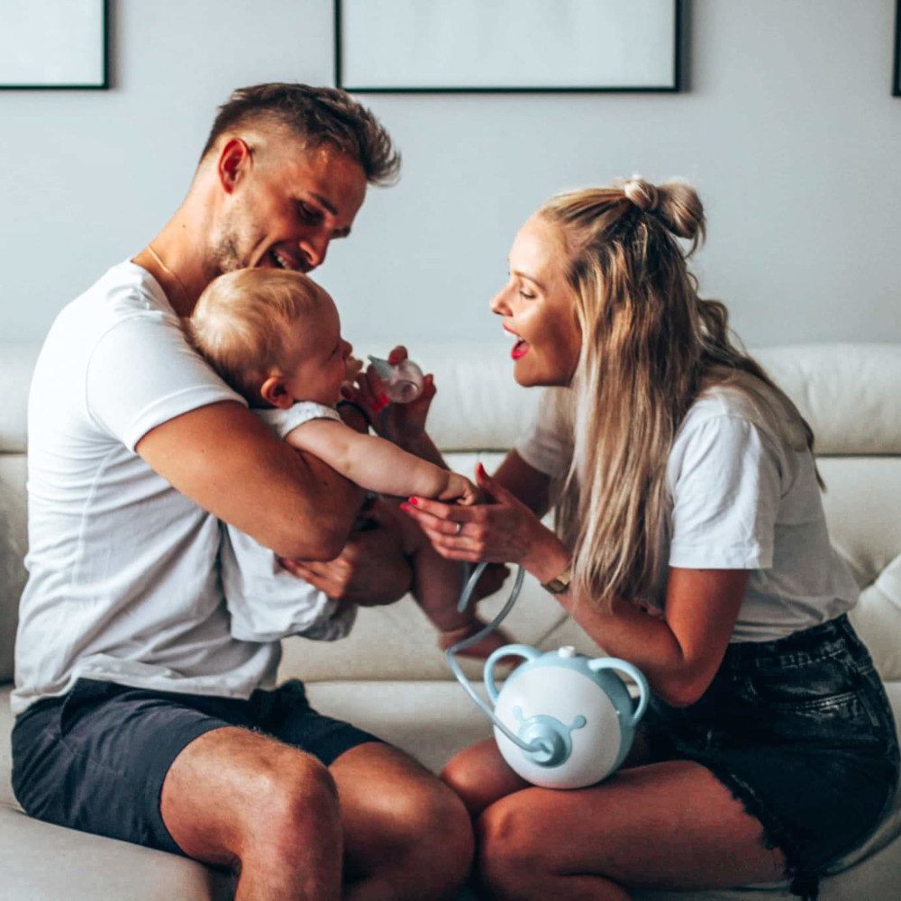 Una mamma e un papà insieme che aspirano il naso del loro bambino con un aspiratore nasale elettrico Nosiboo Pro