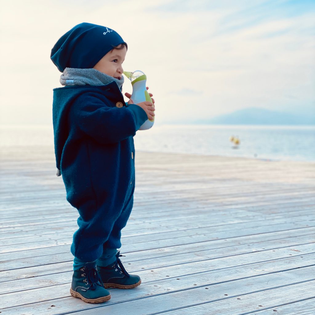 Un petit garçon au bord de l'eau en hiver, tenant un mouche-bébé électrique portatif Nosiboo Go 