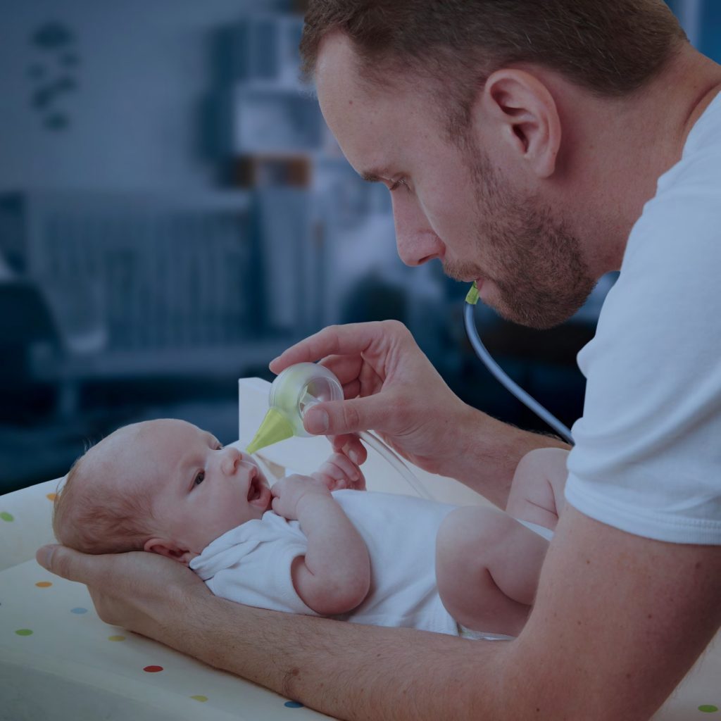 Papà che tiene un neonato e gli aspira il naso con un aspiratore nasale manuale Nosiboo Eco