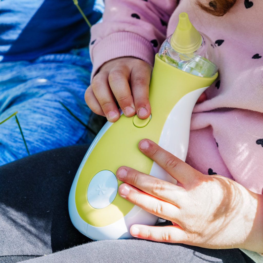 Une petite fille tenant un mouche-bébé électrique portatif Nosiboo Go