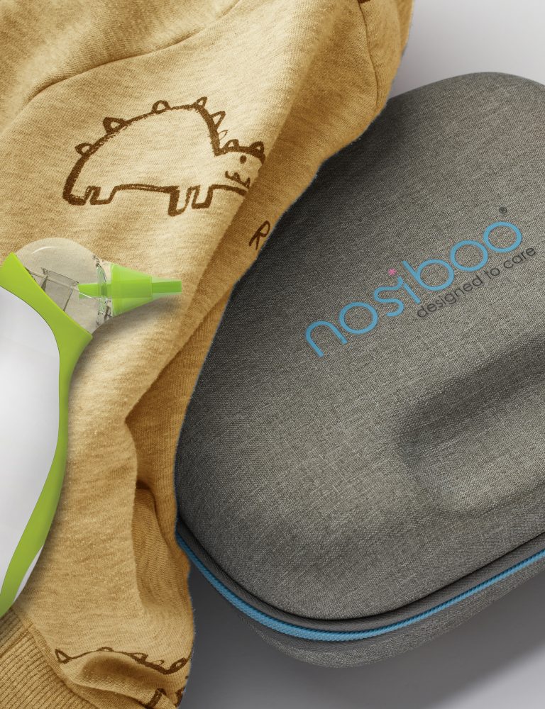 A Nosiboo Bag Go Travel Case placed on a table and covered with a cloth, with a Nosiboo Go portable nasal aspirator next to it.