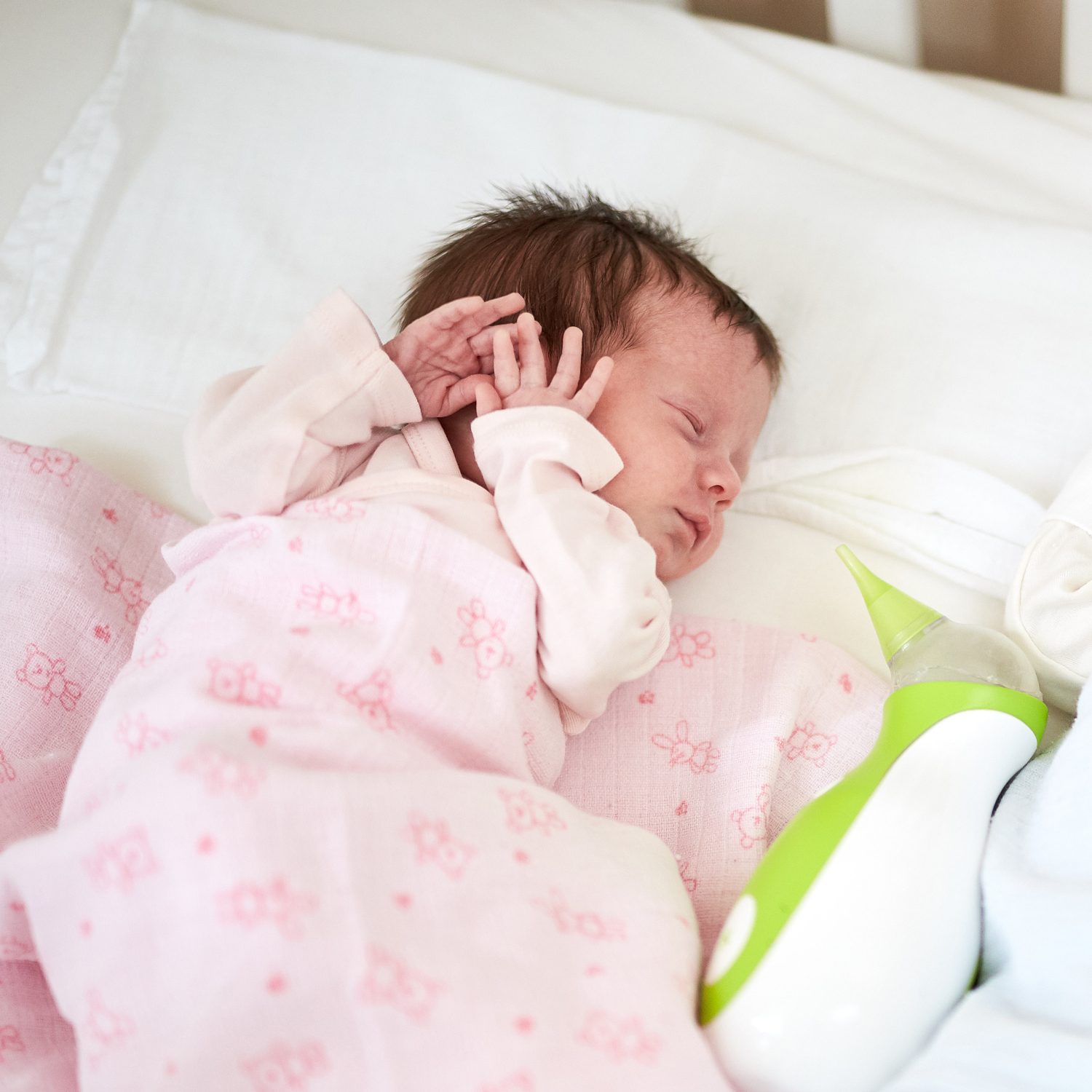 A newborn sleeping in a bed next to a Nosiboo Go portable nasal aspirator.