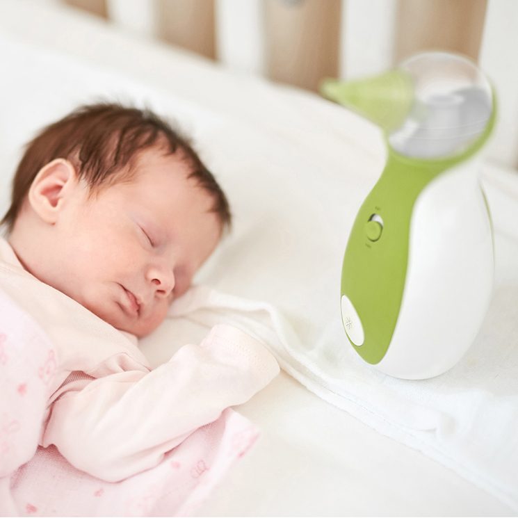 A baby sleeping peacefully in the baby cot bed next to the Nosiboo Go Portable Nasal Aspirator