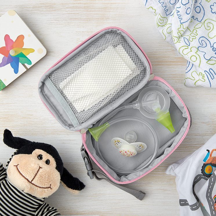 Une trousse de toilette Nosiboo Bag ouverte posée sur une table et contenant le mouche-bébé manuel Nosiboo Eco et d'autres accessoires pour bébé, entourés de jouets et de textiles pour bébé