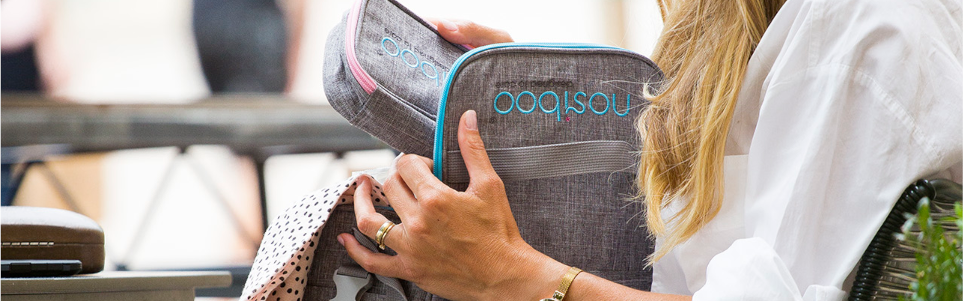 A stylish woman in a café putting the Nosiboo Bag Toiletry Bag into the Nosiboo Bag Baby Organizer