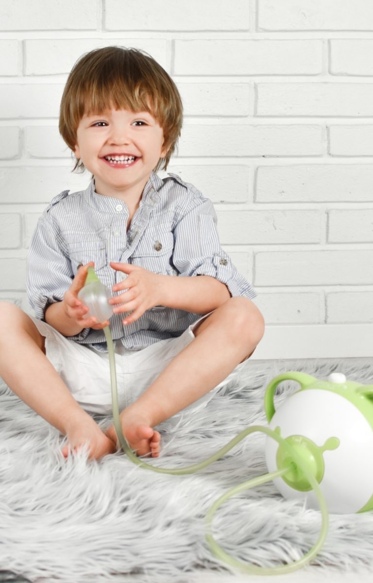 Lächelnder kleiner Junge mit einem Nosiboo Pro elektrischen Nasensauger in der Hand