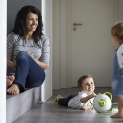 Afficher une photo en taille réelle d'une mère avec deux petits enfants et le mouche-bébé électrique Nosiboo Pro vert dans le couloir de leur maison